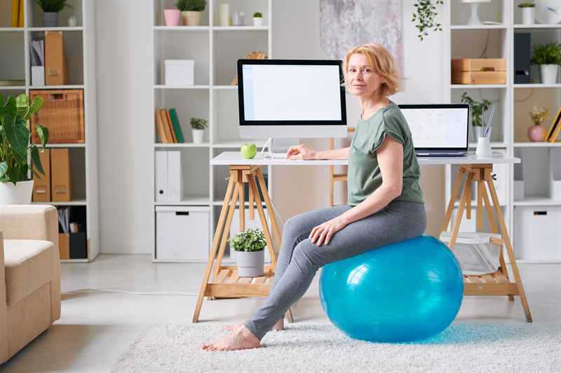 Frau kann auf einem blauen Gymnastikball am Schreibtisch dynamisch sitzen